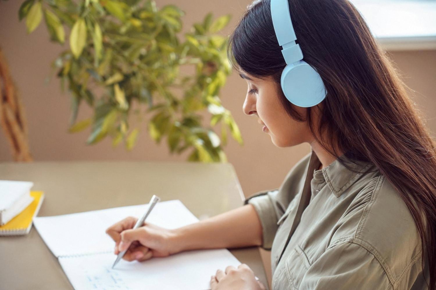 Young woman with headphones taking notes while studying in English
